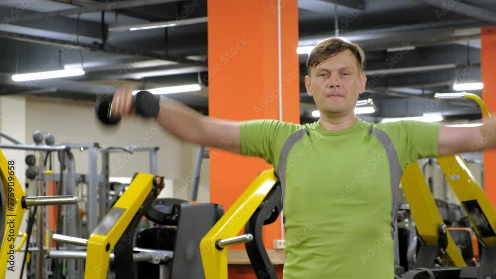 A man doing an exercise on the back delta with dumbbells sitting with a straight grip in a fitness studio A man doing an exercise on the back delta with dumbbells sitting with a straight grip in a fitness studio