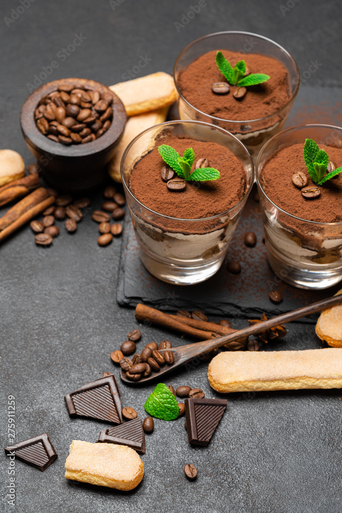 Classic tiramisu dessert in a glass and savoiardi cookies on dark concrete background Classic tiramisu dessert in a glass and savoiardi cookies on dark concrete background