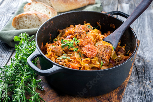 Traditional Polish kraut stew bigos with sausage, meat and mushrooms as closeup in a cast iron pot on an old wooden table
