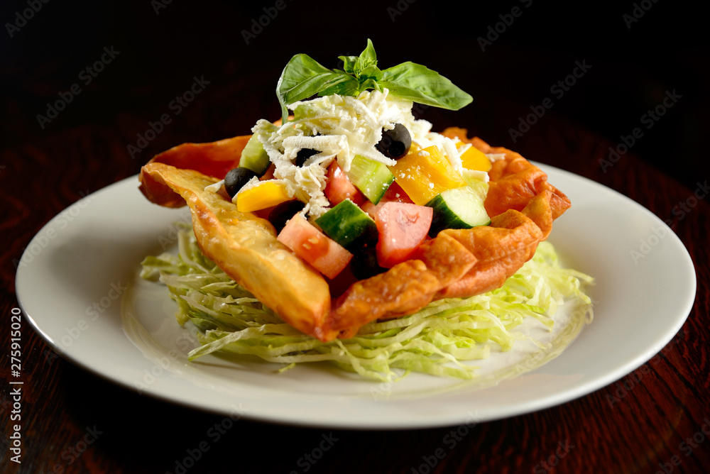 Mixed salad of tomatoes, peppers, olives, basil and cheese in fried tortilla on white plate