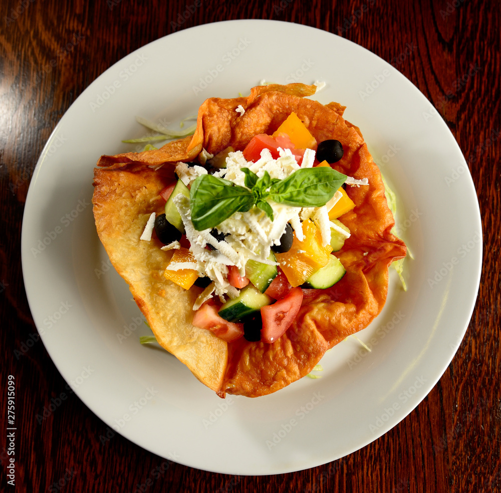 Mixed salad of tomatoes, peppers, olives, basil and cheese in fried tortilla on white plate Mixed salad of tomatoes, peppers, olives, basil and cheese in fried tortilla on white plate