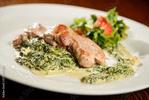 Pork steak with spinach cream sauce and vegetables on white plate