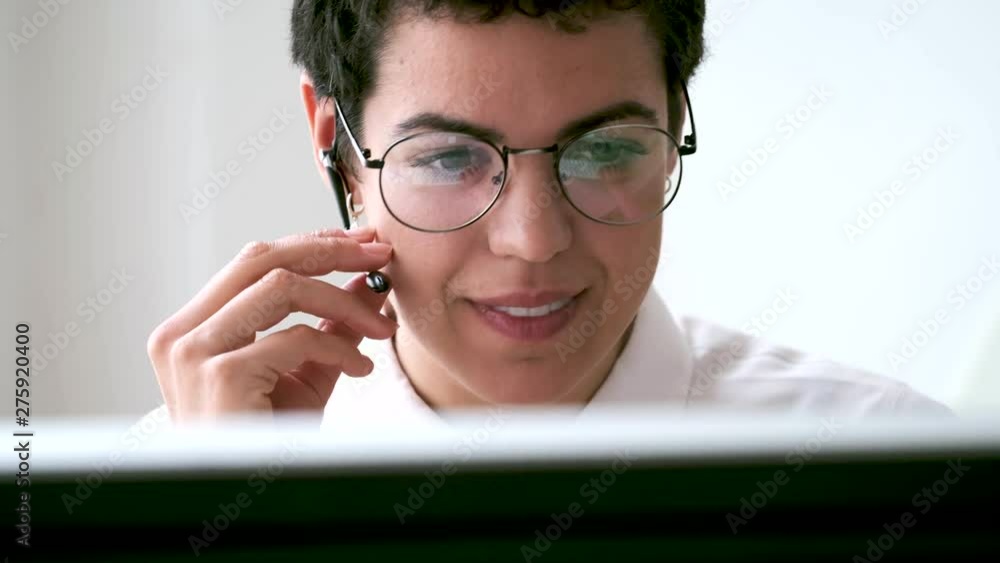 Smiling young business woman using her free hands to make a call while working with her computer in the office. Smiling young business woman using her free hands to make a call while working with her computer in the office.