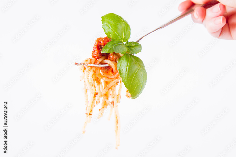 Spaghetti bolognese on a fork decorated with basil on a white background held by female hand	