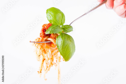 Spaghetti bolognese on a fork decorated with basil on a white background held by female hand 