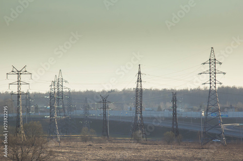 The pylons of high-voltage power lines standing in the middle of the field against the backdrop of forests. A transmission tower, power tower structure at 110 kilovolts. Industry and energy systems.