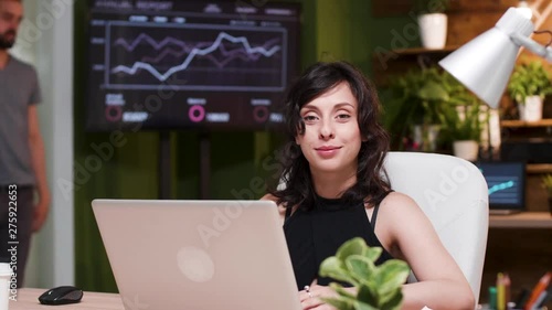 Young businesswoman sitting at the desk, lookint at camera and smiling photo