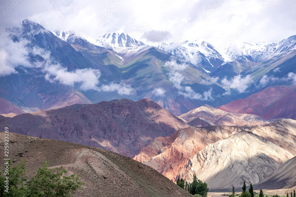View of the colorful mountains and snow-capped peaks with clouds on them. Travel Kyrgyzstan