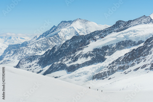 Swiss Alps mountain range landscape full of snow in winter, with group of traveler trekking to summit