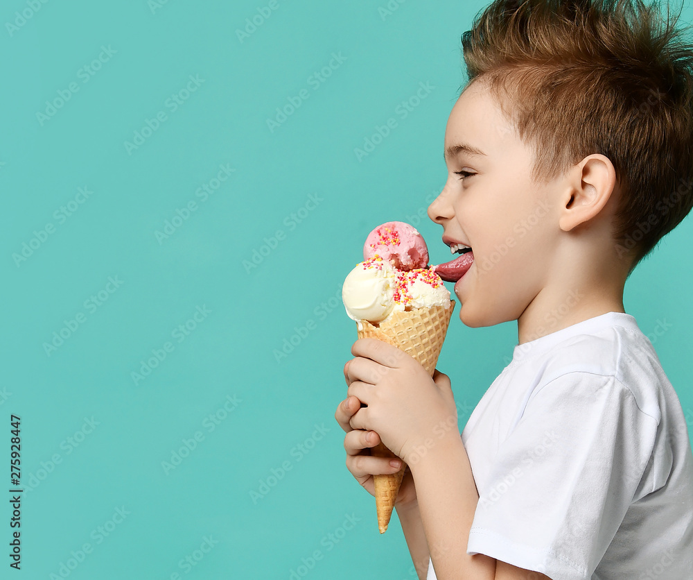 Baby boy kid hold three scoops of strawberry and vanilla ice cream in waffles cone on blue mint background