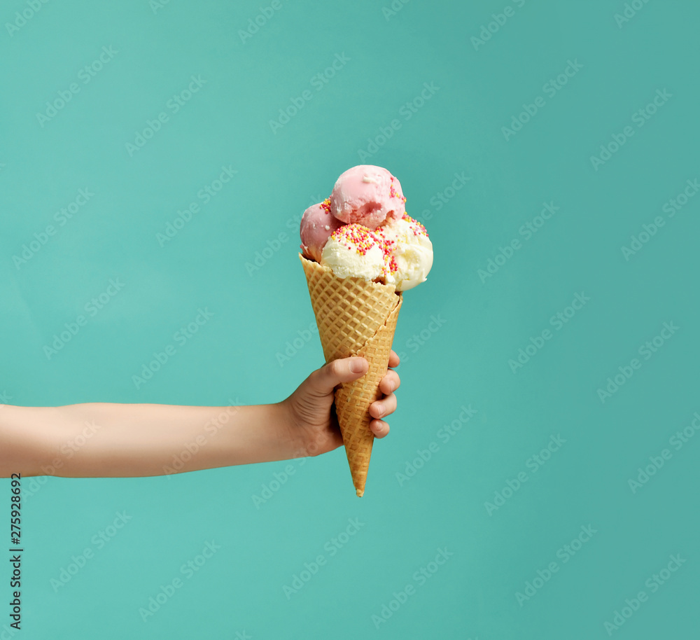 Baby kid hand holding big ice-cream in waffles cone on blue