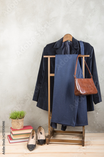 Shopping and style concept - clothes rack with trendy blue jacket and striped pants, bag and shoes on wooden floor and grey concrete background