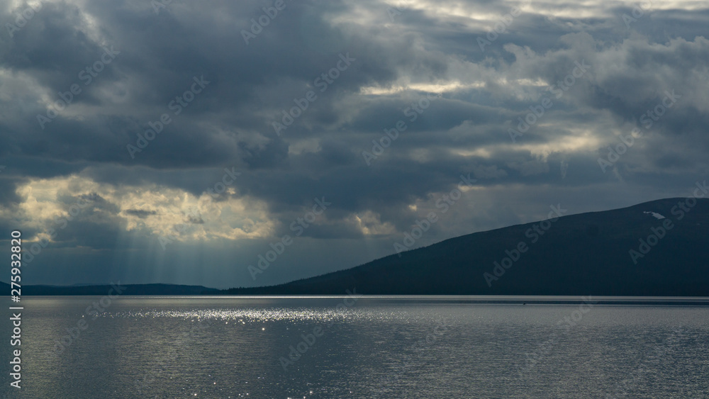 Sunlight through the clouds over the rocky northern lake