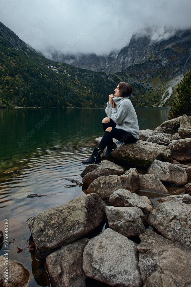 Girl sitting on rocks near lake. Tatra mountains landscape in Poland, Zakopane. Mountain landscape in Eastern Europe.