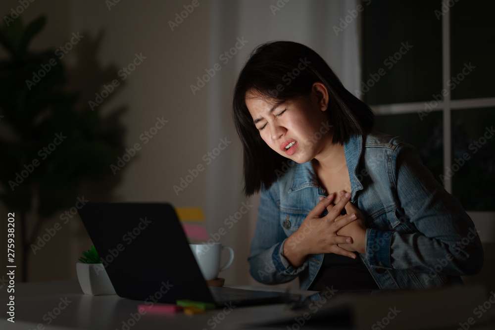 Candid of young asian woman or student work late sitting on desk with computer laptop at home office. Risk of occupational burnout stress syndrome in heart attack disease of asian people concept. Candid of young asian woman or student work late sitting on desk with computer laptop at home office. Risk of occupational burnout stress syndrome in heart attack disease of asian people concept.