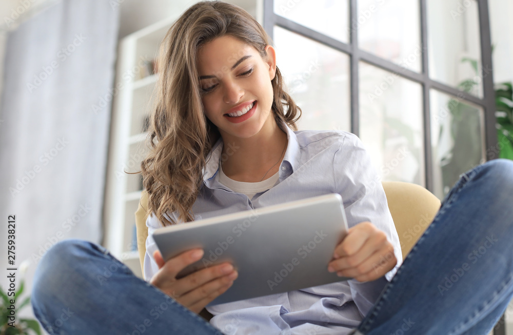 Smiling young female sitting in the armchair in the living room and using with her tablet. Smiling young female sitting in the armchair in the living room and using with her tablet.