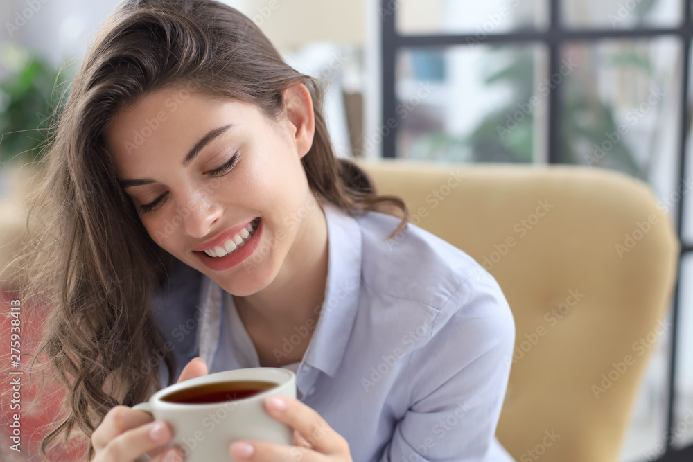 Smiling young female sitting in the armchair in the living room, holding a cup of coffee. Smiling young female sitting in the armchair in the living room, holding a cup of coffee.