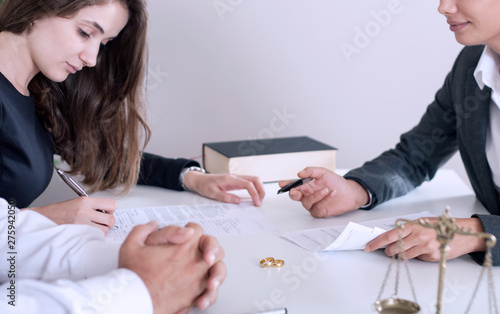 partial view of lawyer and client sitting at table with divorce decree and wedding rings