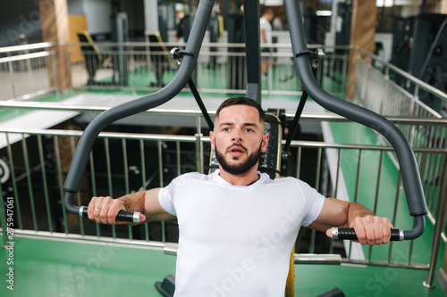 A young athlete trains in the gym. Bodybuilder trains the muscules of the chest photo