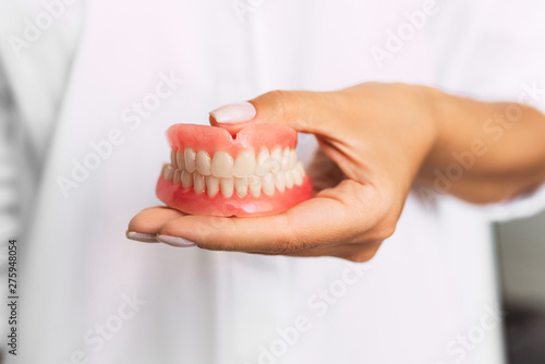 Dental prosthesis in the hands of the doctor close-up. Dentist holding ceramic dental bridge. Front view of complete denture. Dentistry conceptual photo. Prosthetic dentistry. False teeth