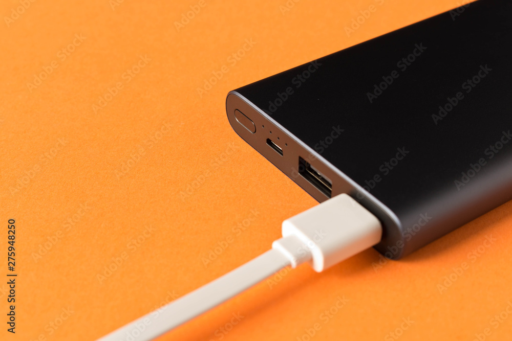 Black power Bank with adapter for charging mobile devices on a orange background. Black power Bank with adapter for charging mobile devices on a orange background.