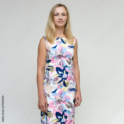 Portrait of a pretty beautiful adult female 35 years old blonde on a white background in a light dress with a pattern. Standing in front of the camera, smiling.