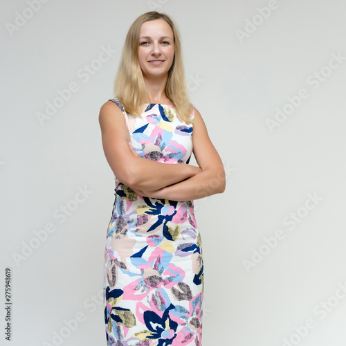 Portrait of a pretty beautiful adult female 35 years old blonde on a white background in a light dress with a pattern. Standing in front of the camera, smiling.