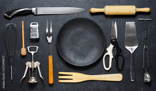 Wooden and metal kitchen utensilsand a black plate . Tools for cooking. Dark background. Flat lay