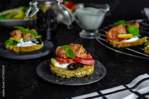 small canape with pink salmon fish, cucumber, tomato, olive and lemon on a black background. dark food photo