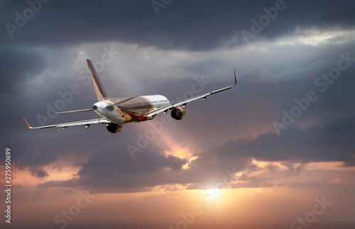 passenger plane flying in the stormy dramatic sky. the sun shines from behind the clouds. the plane flies