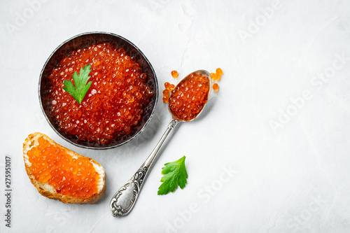 Delicious red caviar in black bowl on a light concrete background. Top view with copy space. Flat lay photo