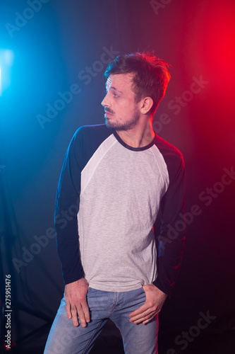 Slim young bearded hipster man in casual clothes posing on a red blue background. Concept of style and confidence.