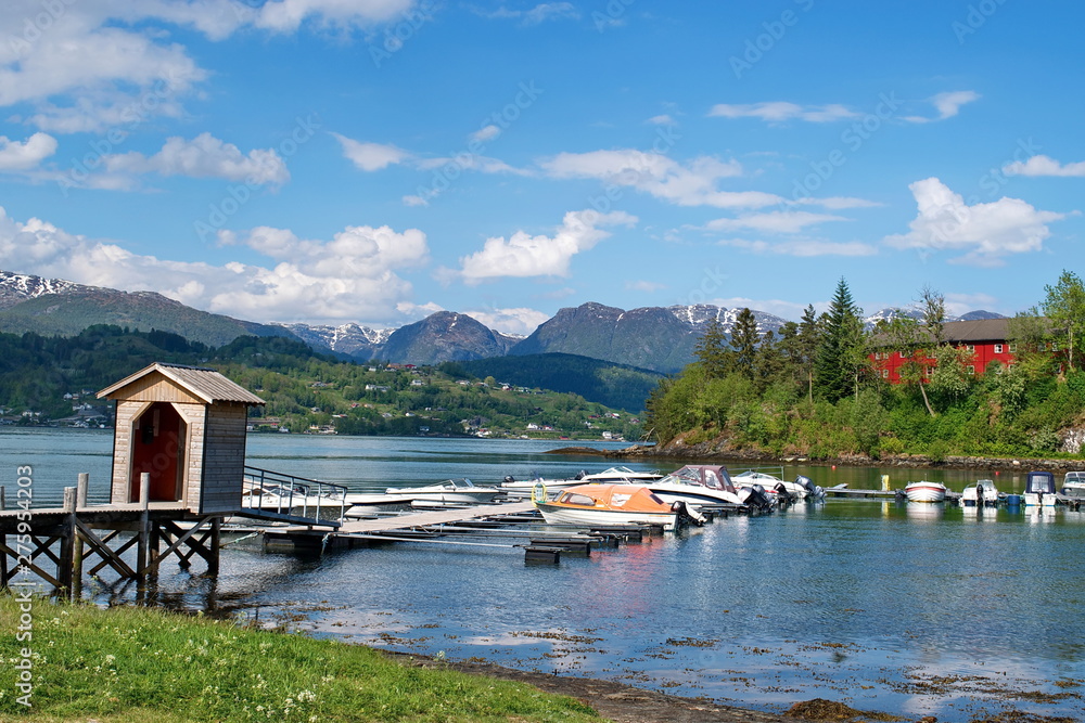 Fototapeta premium Norwegian landscape with Hardanger fjord, mountains, boats, pier , flowers and cloudy sky in Norway