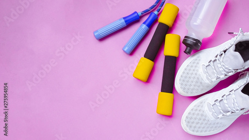 Fitness background of Equipment for gym and home, Sports shoes, Jump rope, dumbbells, mat, water on pastel pink background top view for copy space