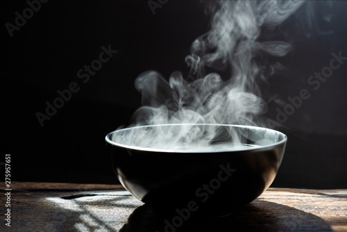 Steam of hot soup with smoke wood bowl on dark background.selective focus