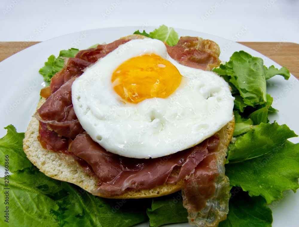 Fried egg with bread, ham, and salad on white dish, wooden table