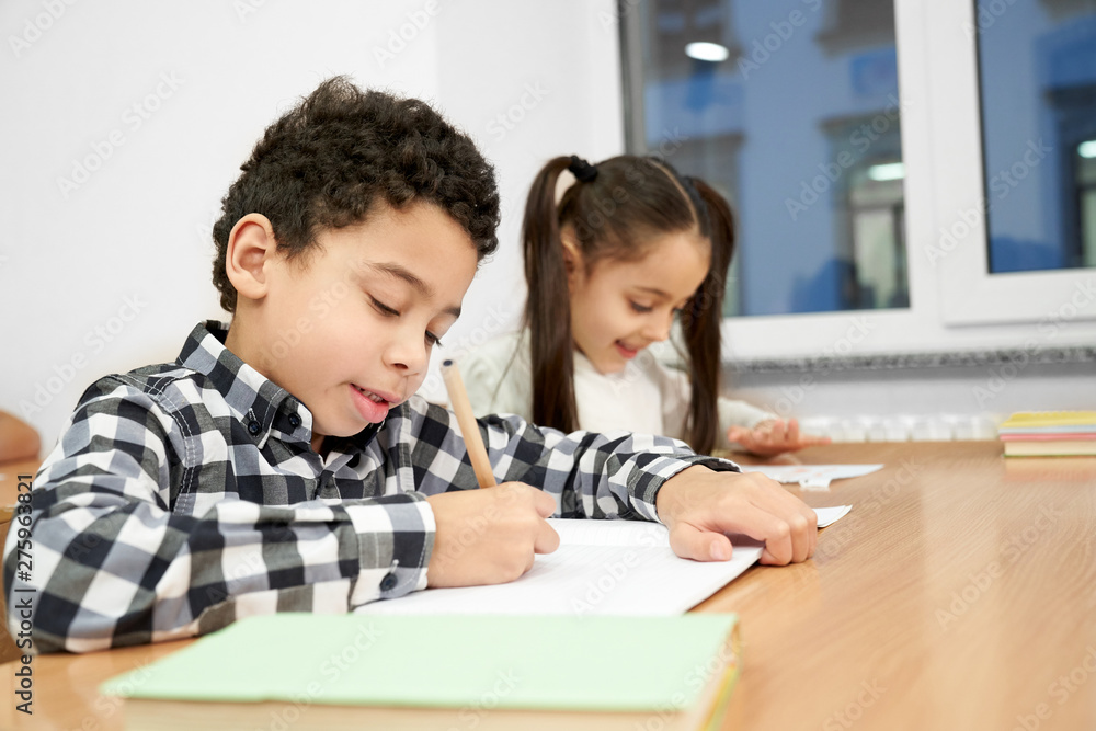 Concentrated boy sitting at table and writing in copybook Concentrated boy sitting at table and writing in copybook