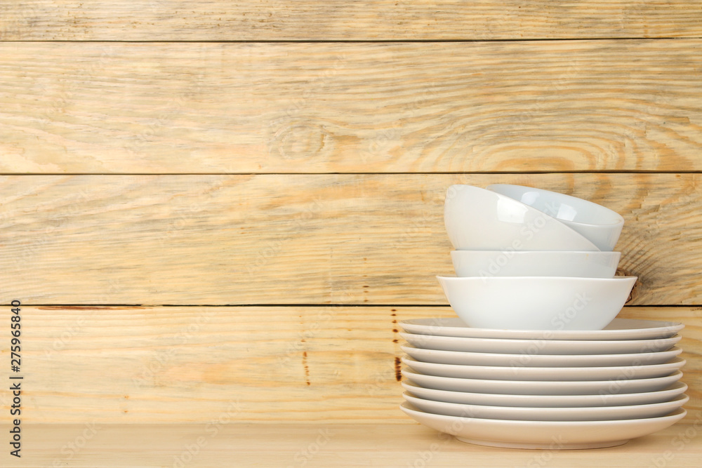 Piles of white ceramic tableware, plates, saucers and cups on a natural wooden background. kitchenware. Piles of white ceramic tableware, plates, saucers and cups on a natural wooden background. kitchenware.