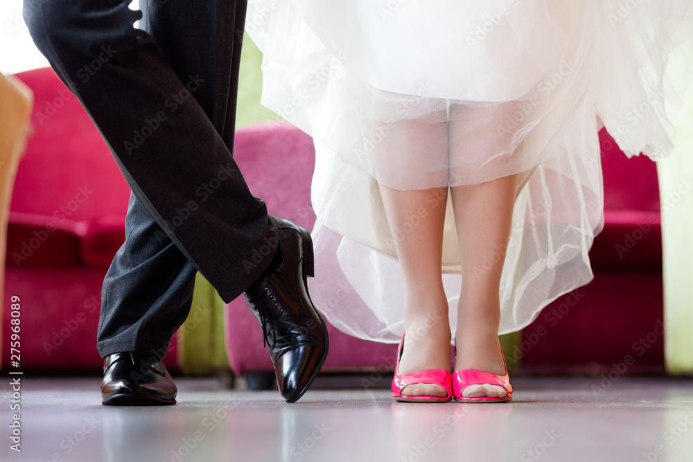 Legs of the groom in black shoes and trousers and brides in crimson heels with a snow-white hem of a wedding dress Legs of the groom in black shoes and trousers and brides in crimson heels with a snow-white hem of a wedding dress