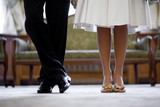 Legs of the groom in black shoes and trousers and brides in beige heels with snow-white hem of a wedding dress