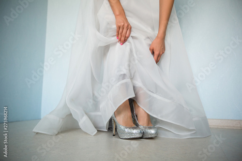 Bride's legs in silver heels with the raised hem of a wedding dress