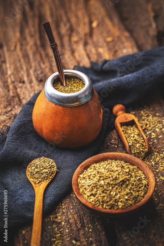 Yerba mate in calabash with bombilla and dry herb in wooden bowl on wooden background photo
