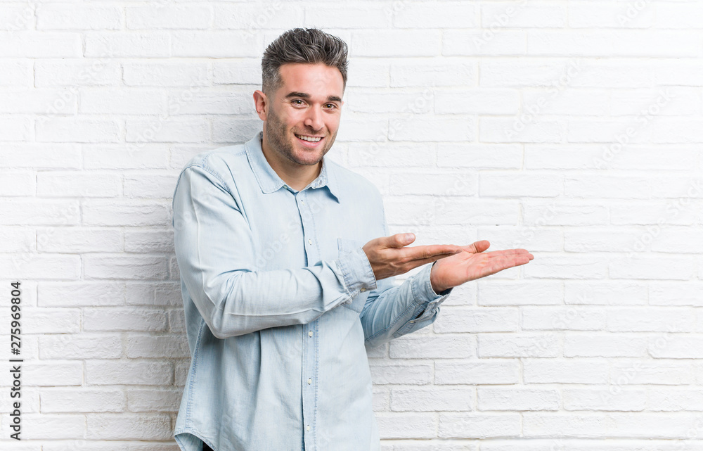 Young handsome man against a bricks wall holding a copy space on a palm. Young handsome man against a bricks wall holding a copy space on a palm.