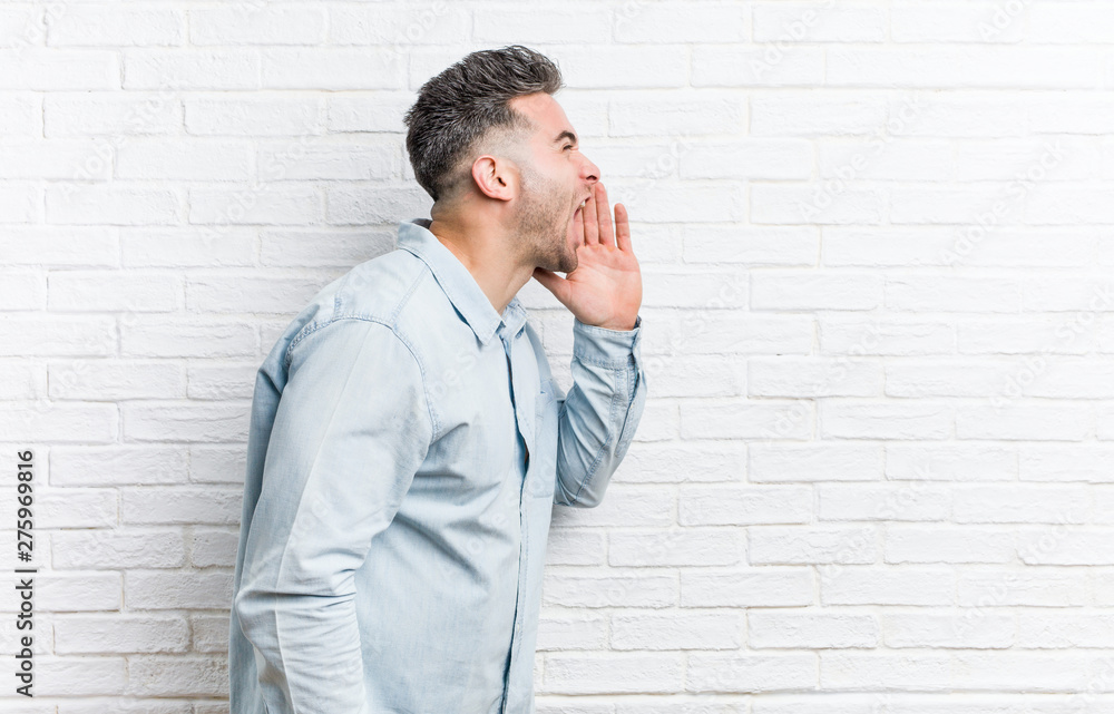 Young handsome man against a bricks wall shouting and holding palm near opened mouth. Young handsome man against a bricks wall shouting and holding palm near opened mouth.