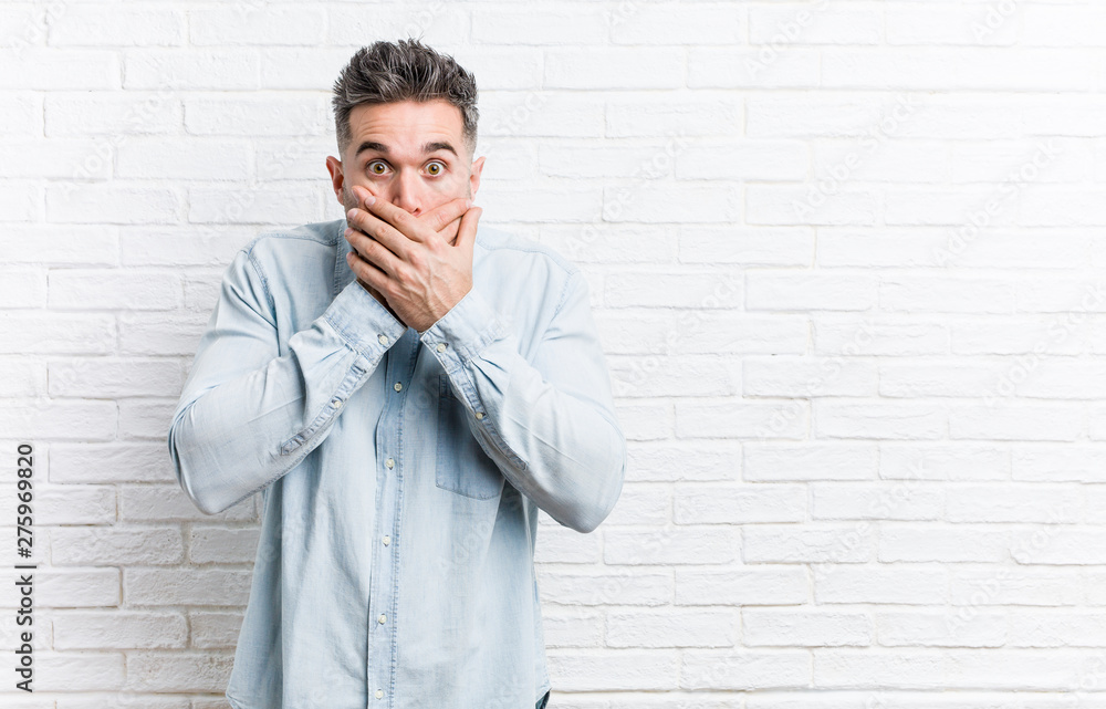 Young handsome man against a bricks wall shocked covering mouth with hands. Young handsome man against a bricks wall shocked covering mouth with hands.