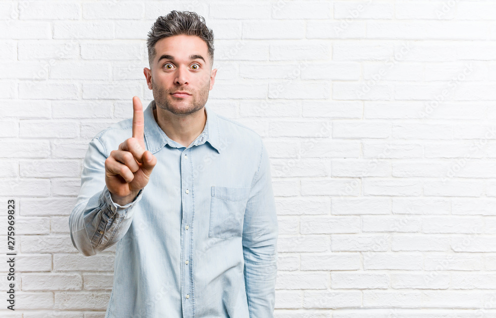 Young handsome man against a bricks wall showing number one with finger. Young handsome man against a bricks wall showing number one with finger.