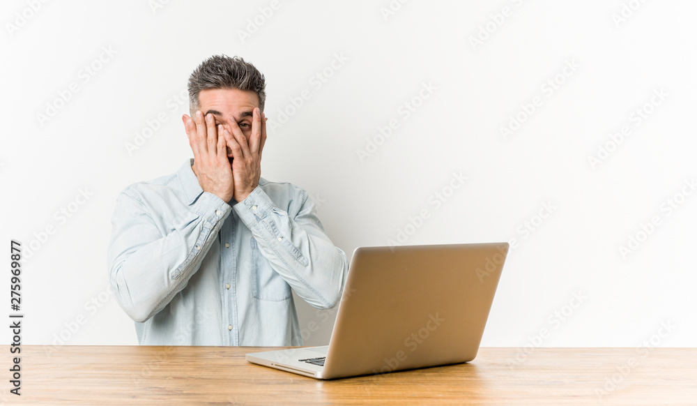 Young handsome man working with his laptop blink through fingers frightened and nervous. Young handsome man working with his laptop blink through fingers frightened and nervous.