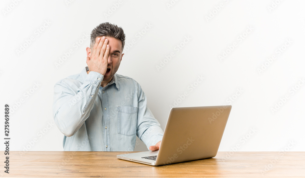 Young handsome man working with his laptop having fun covering half of face with palm. Young handsome man working with his laptop having fun covering half of face with palm.