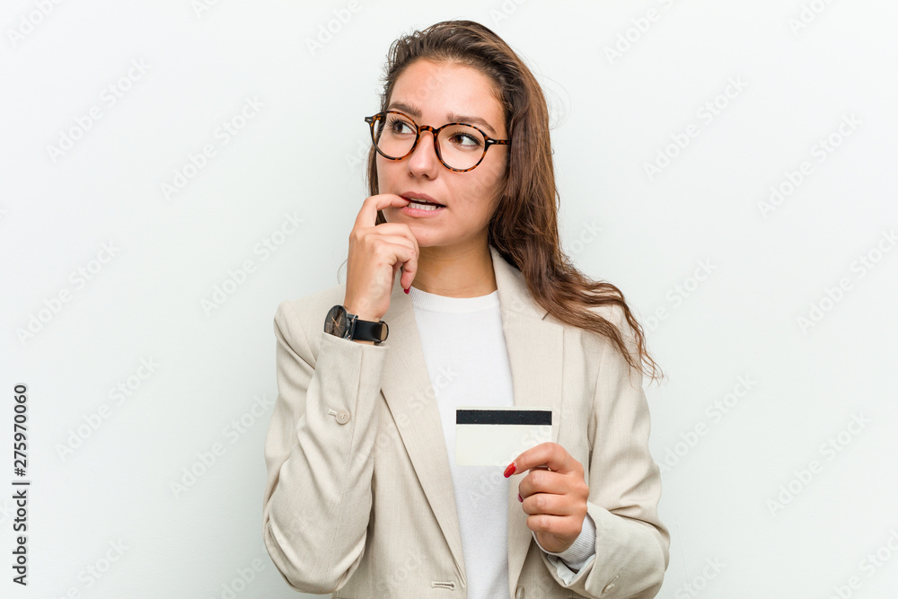 Young european business woman holding a credit card relaxed thinking about something looking at a copy space. Young european business woman holding a credit card relaxed thinking about something looking at a copy space.