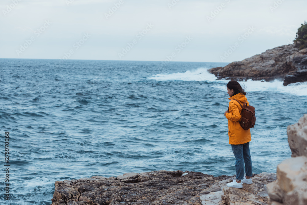 woman standing on the cliff looking on storming sea in yellow raincoat